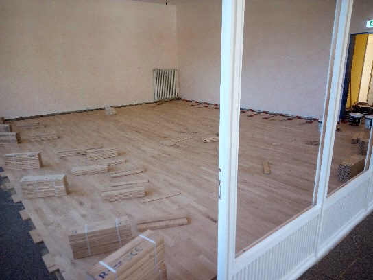 Verlegung von Vollholzparkett für einen Eurythmieraum durch Boden-Frost Parkett unter Anleitung von Wulf Frost in Osterholz-Scharmbeck, mit gestapelten Parkettstäben und vorbereitetem Boden.